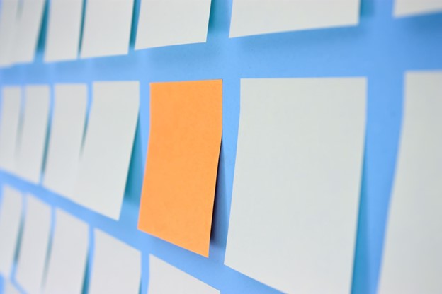 Image of a bright colored sticky note within rows of white sticky notes on a wall
